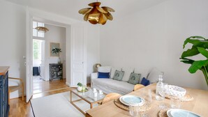 A modern living room with a wooden dining table set for a meal, a sofa with cushions, and a hanging light fixture. - Flat in the town centre - 270m  l'Ecluse beach (Dinard)