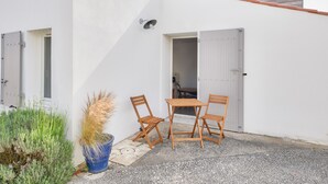 A small patio with a table and two chairs, a potted plant, and a white building with a grey door. - Quiet location - 5min from La Terrière beach (La Tranche-sur-Mer)