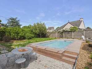 A backyard with a swimming pool, a patio with a table and chairs, and a wooden deck. - Unique house for 6 adults and 2 children (Erquy)
