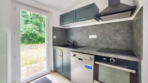 A compact kitchen with a dishwasher, oven, and a window overlooking a grassy area. - 850 from de beach, new house for 6 in the wood (Longeville-sur-Mer)