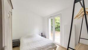 A bedroom with a bed, a bedside table, a lamp, and a view of the outdoors through a sliding door. - 850 from de beach, new house for 6 in the wood (Longeville-sur-Mer)