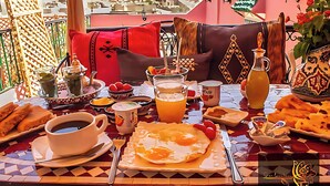 A breakfast table with various dishes, including eggs, bread, and beverages, set on a balcony with a city view. - Riad Mounana luxurious palace & spa  (Fes)