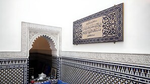 A room with intricate geometric tile patterns, a sofa with colorful cushions, and a framed Arabic calligraphy piece on the wall. - Riad Mounana luxurious palace & spa  (Fes)