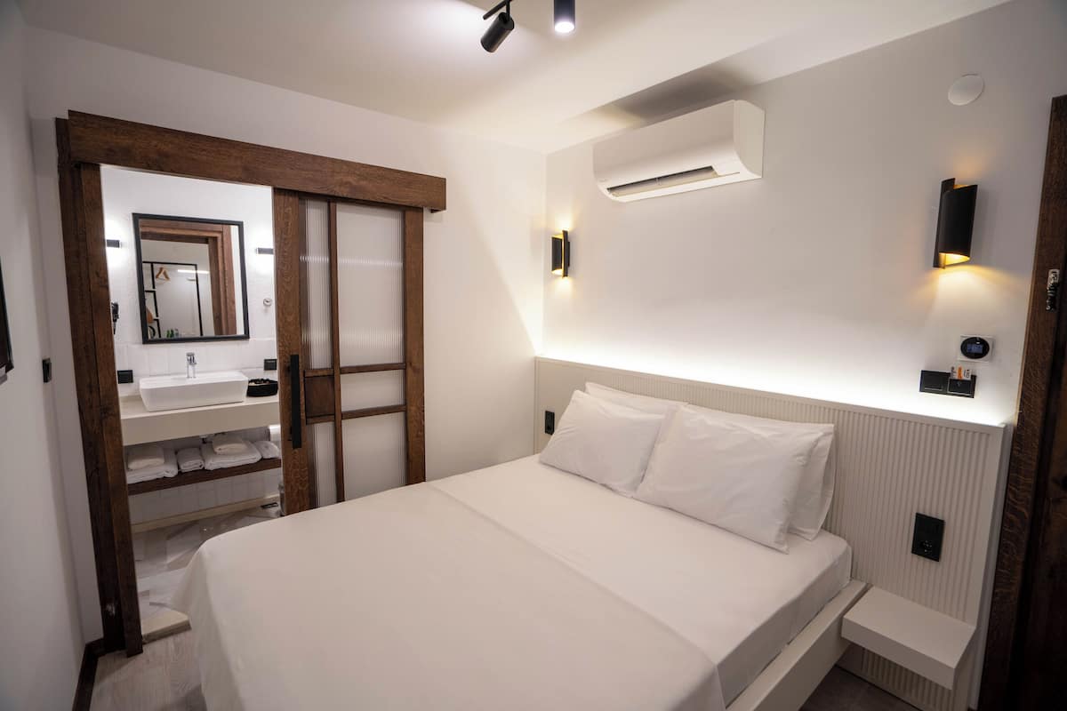 A modern hotel room with a large bed, a built-in wardrobe, a vanity with a mirror, and wall-mounted lighting.