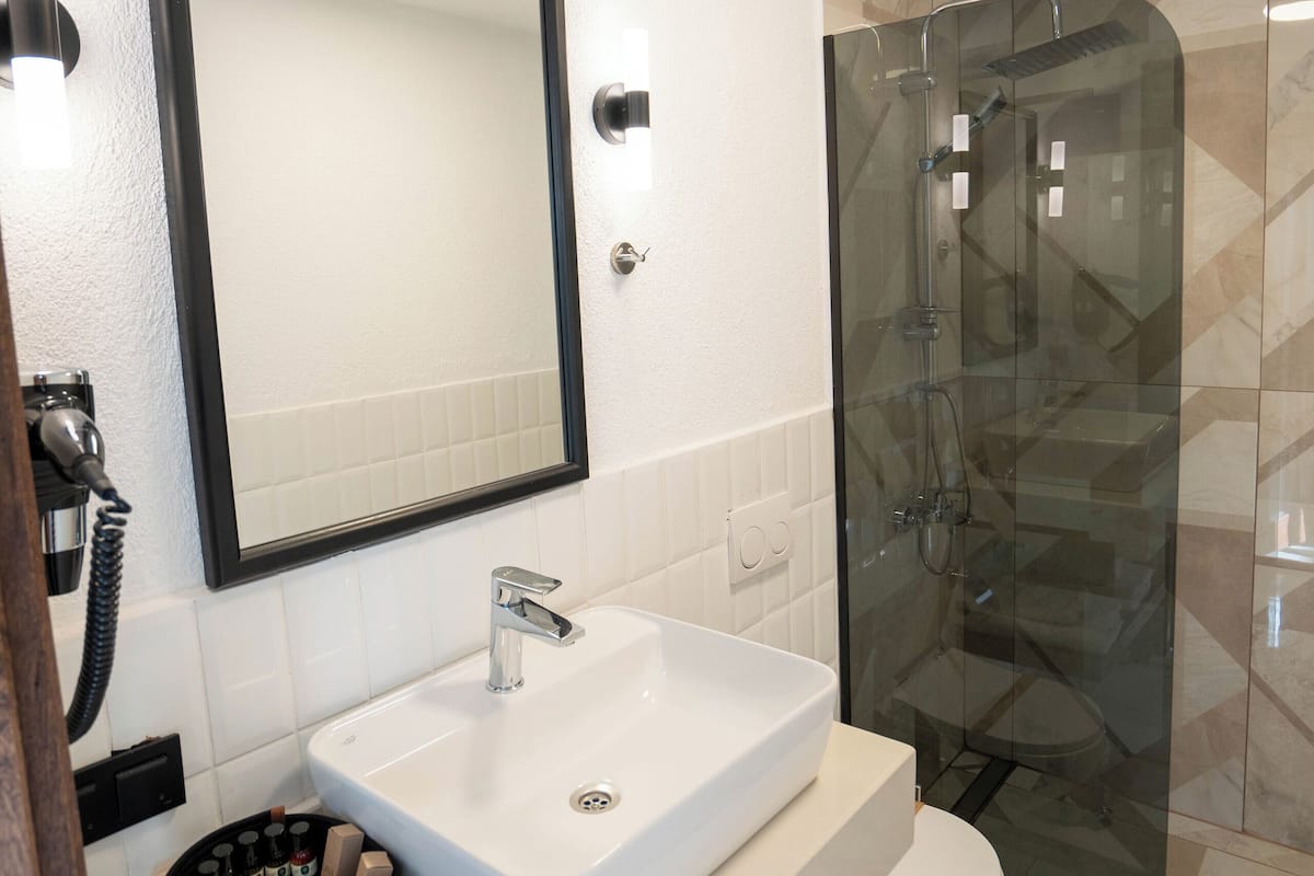 A modern bathroom with a white sink, a large mirror, a glass-enclosed shower, and a toilet.