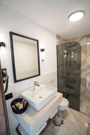 Un baño moderno con un lavamanos blanco, un espejo grande, una ducha con cerramiento de vidrio y un inodoro.