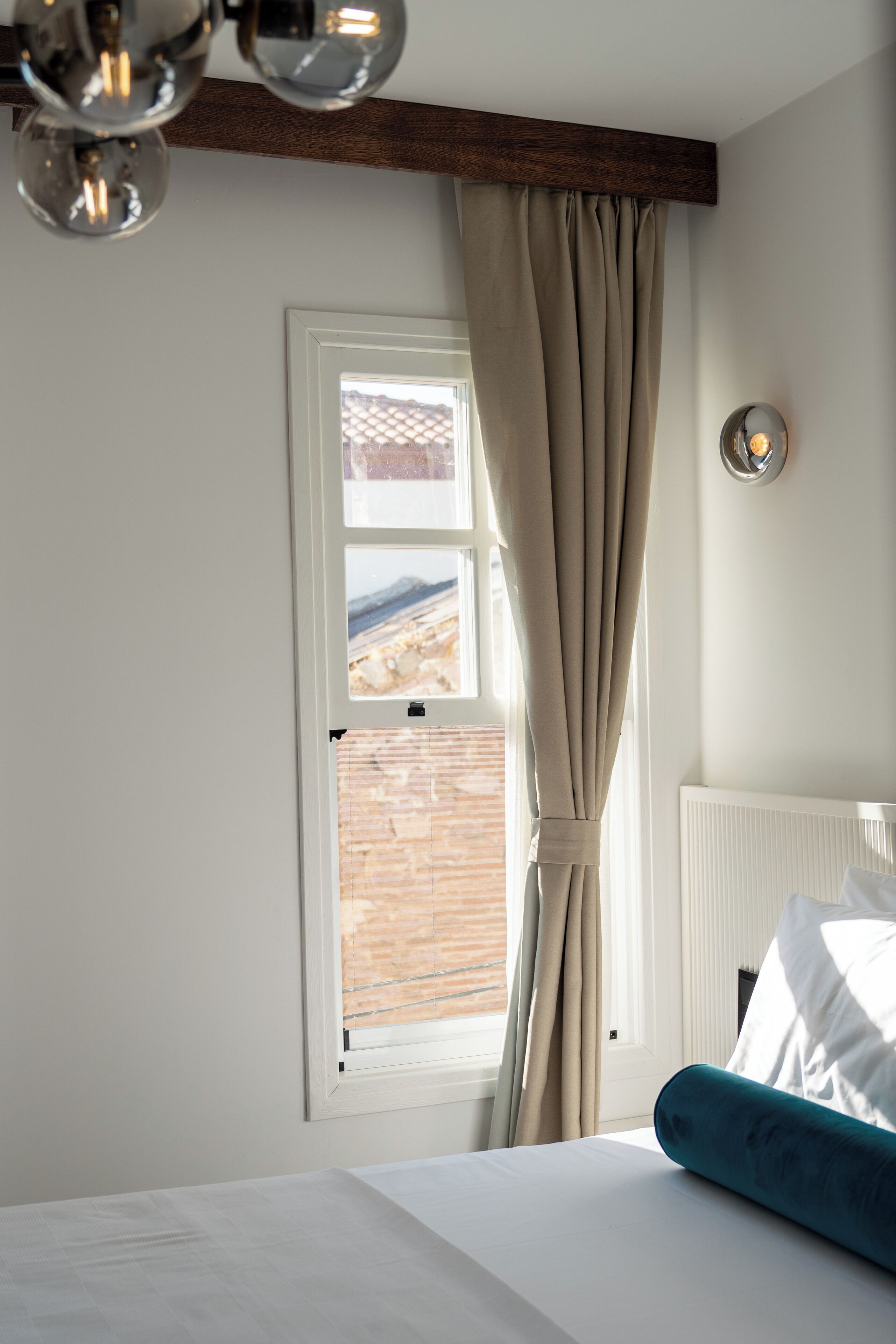 Une chambre à coucher avec un lit, une fenêtre avec des rideaux, une vue sur un mur de briques et un luminaire au plafond.