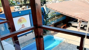 Udsigt fra en balkon over et swimmingpool med stentilfliser, en blå væg med et muralmaleri, og en parkeret bil.