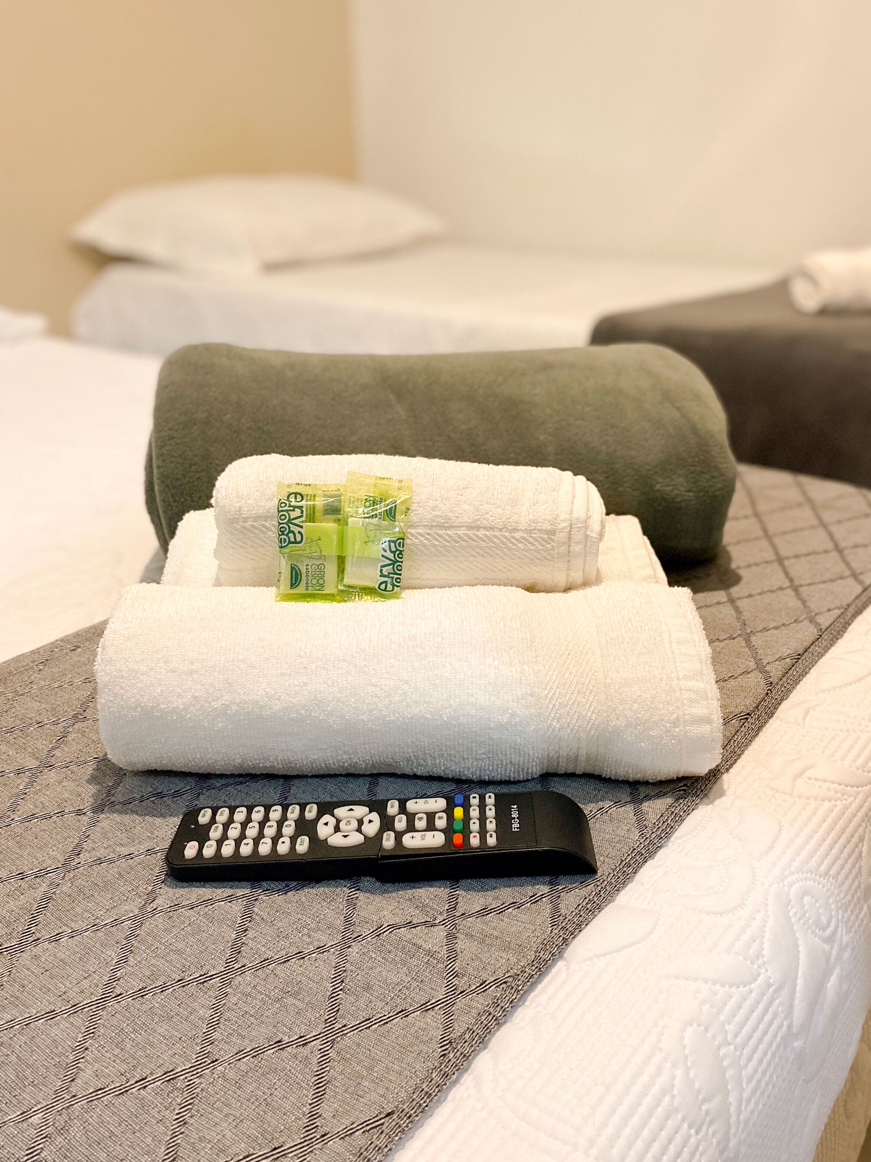Una cama bien hecha con una toalla blanca doblada, una almohada verde y un control remoto sobre un edredón estampado.