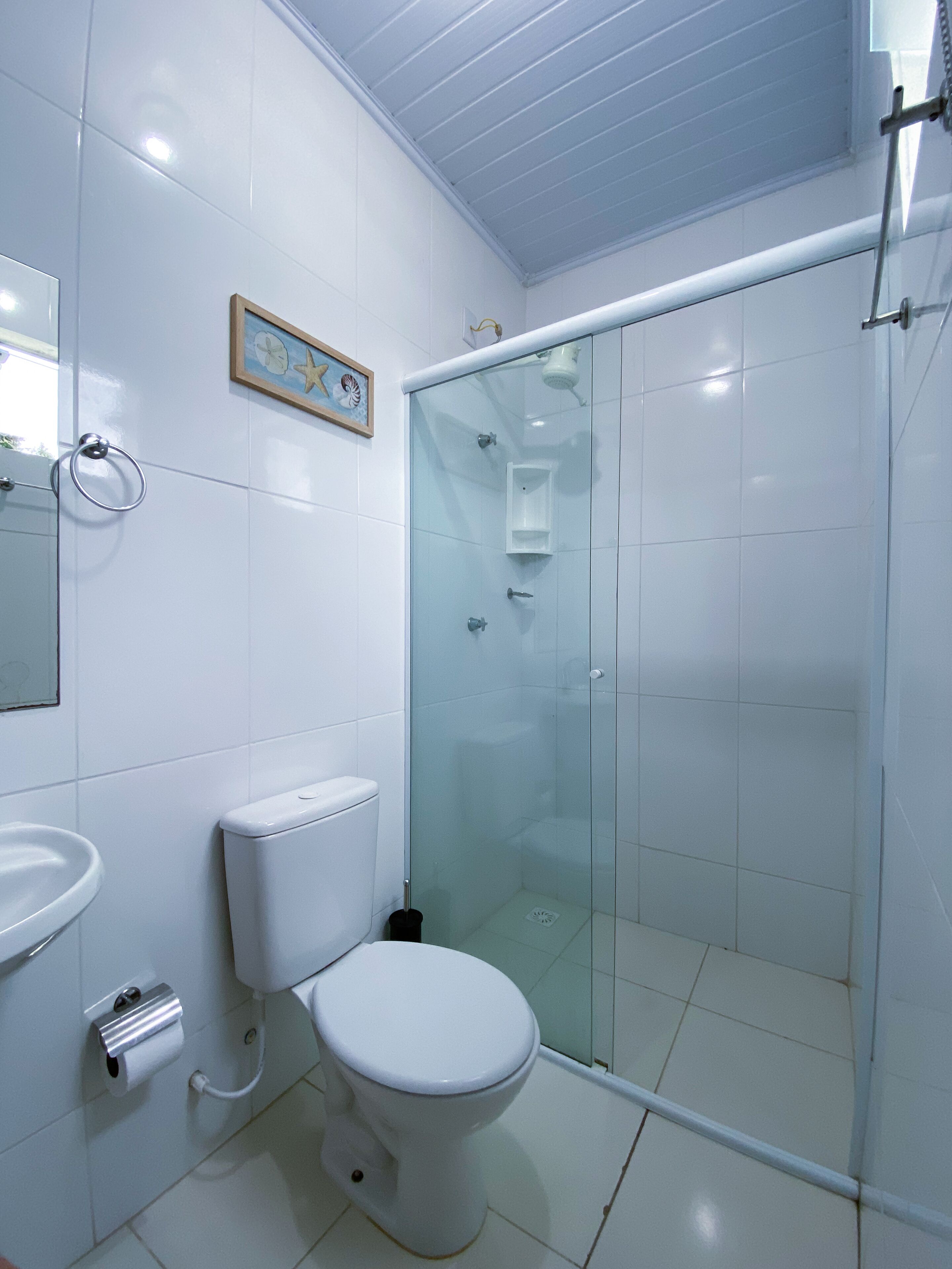 Un baño con inodoro, lavamanos y cabina de ducha con mampara de vidrio.