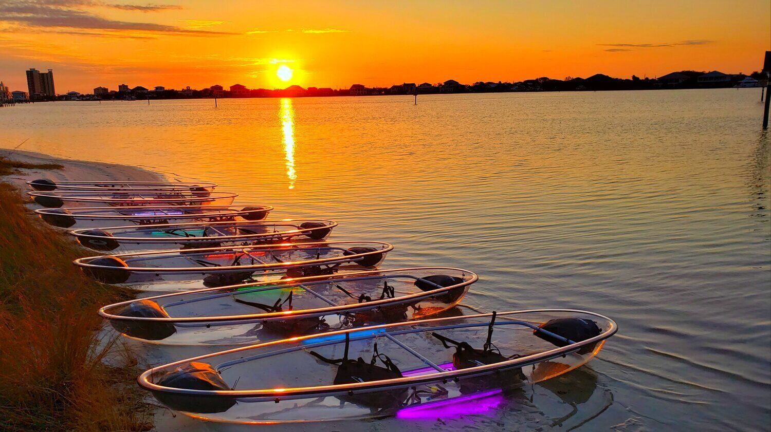 Une rangée de canoës alignés le long d’une rive, au coucher du soleil.