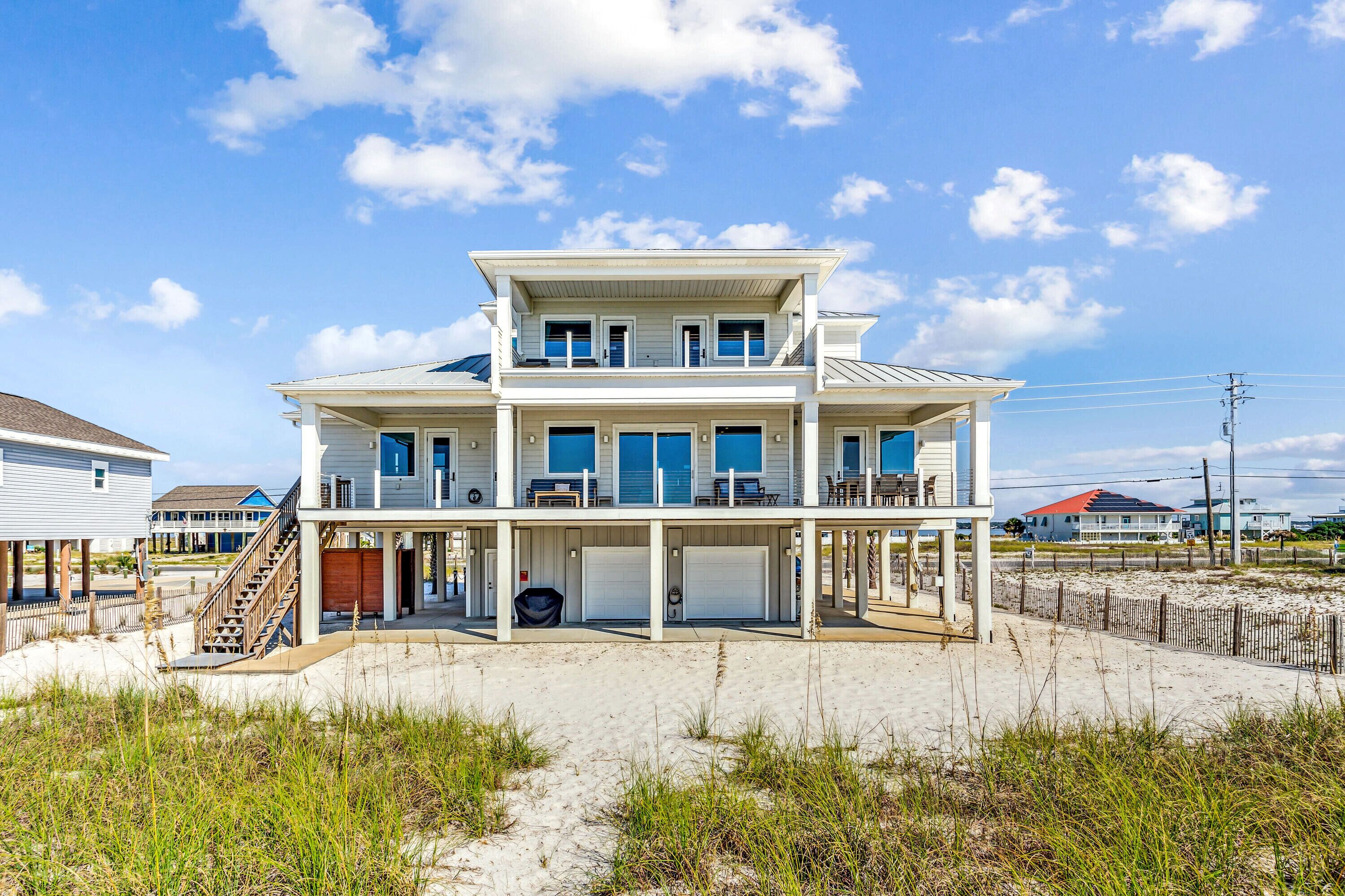 Een twee verdiepingen tellend huis aan het strand, met een overdekte veranda en een trap naar de bovenverdieping.