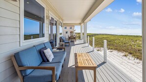 Une terrasse couverte avec un canapé et une table, offrant une vue sur la plage et les dunes.