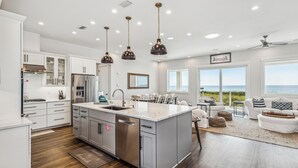 Une cuisine moderne dotée d’un grand îlot central, d’appareils électroménagers en acier inoxydable et de luminaires suspendus.
