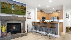 Eine moderne Küche mit Kamin aus Stein, Holzschränken und einer Bar mit Hockern.