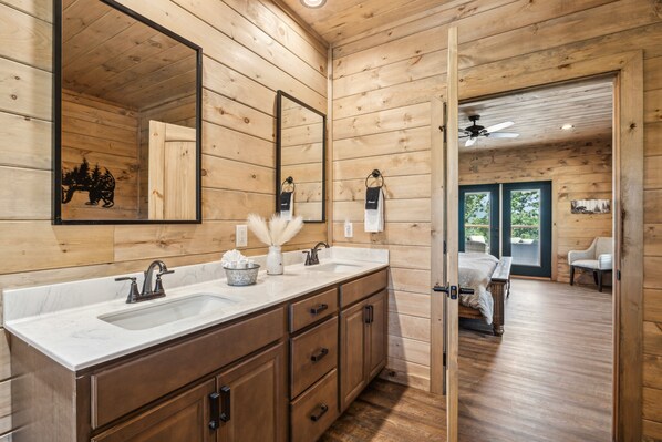 A wooden cabin bathroom with a large mirror, two sinks, and a vanity.