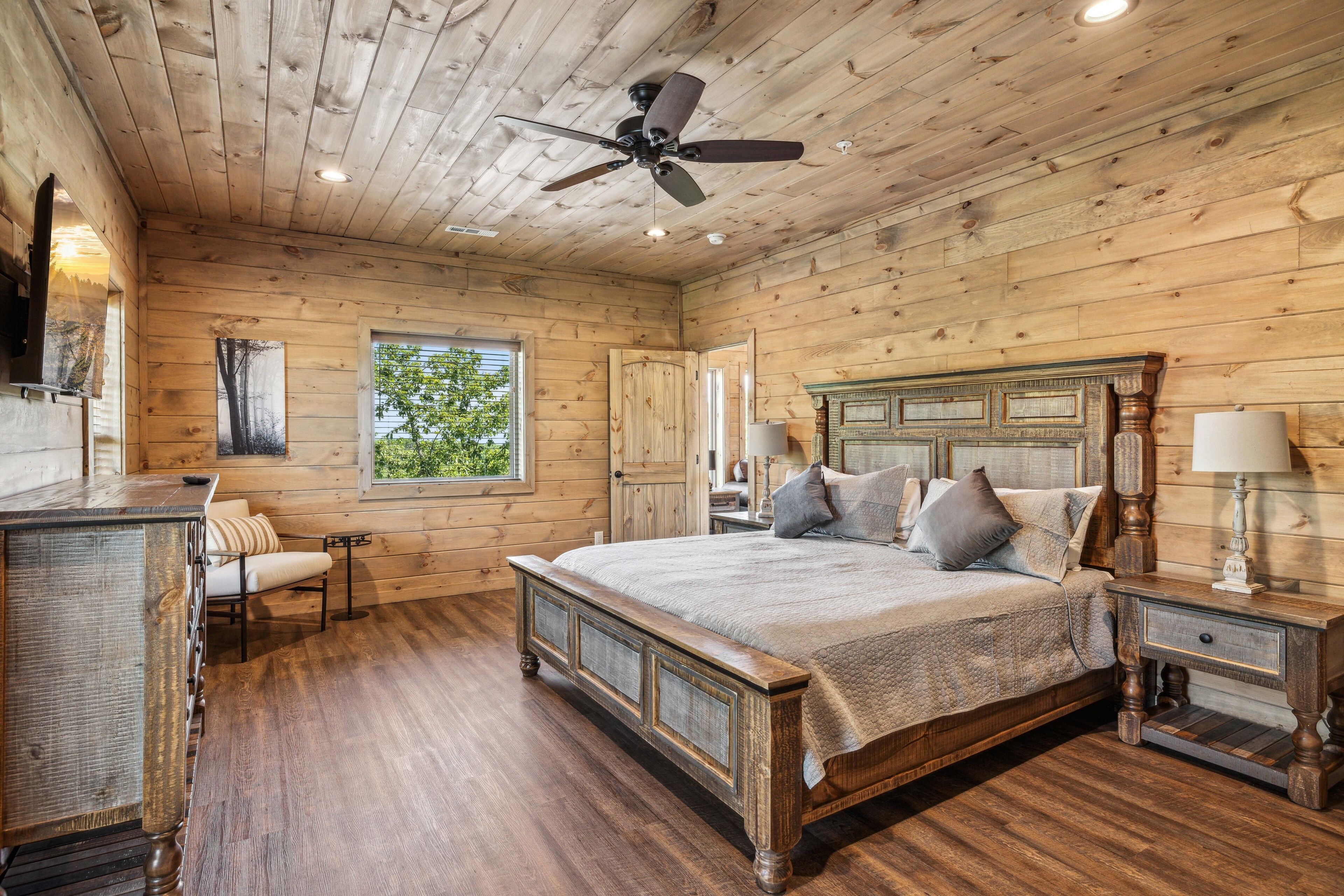 A wooden cabin bedroom with a large bed, a desk, and a chair.