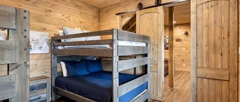 Habitación tipo cabaña de madera con literas, un armario y suelo de madera.