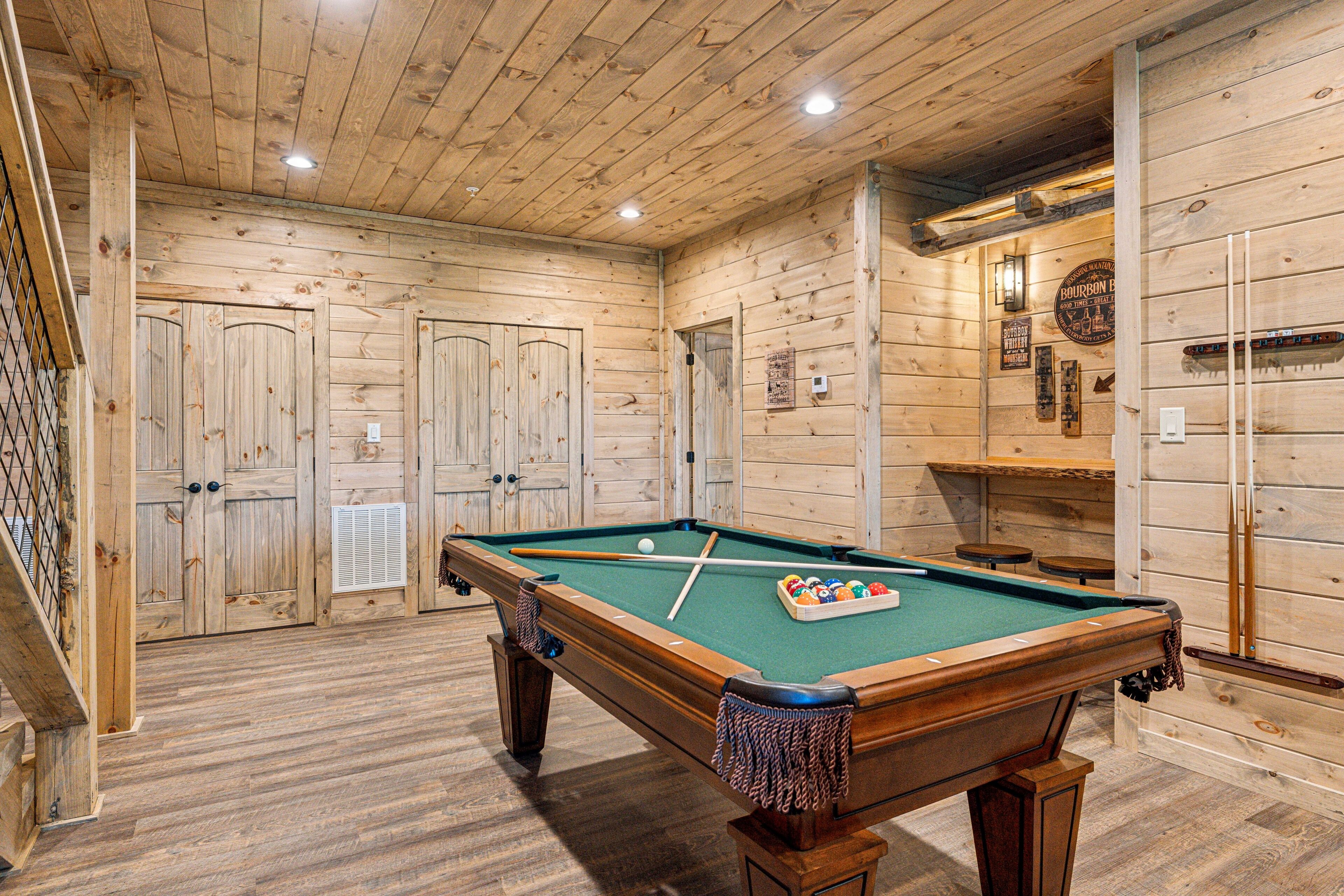 A wooden pool table in a room with wooden walls and a staircase.