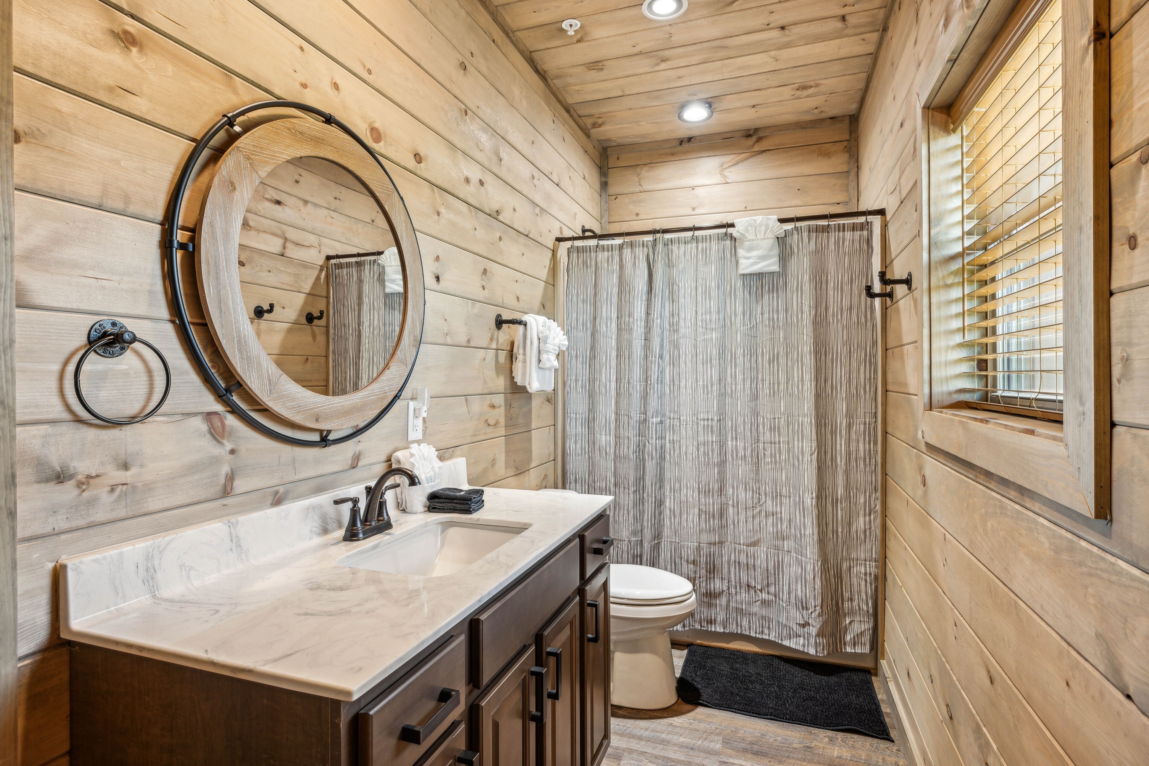 Un baño de cabaña de madera con un espejo redondo, un lavabo y un inodoro.