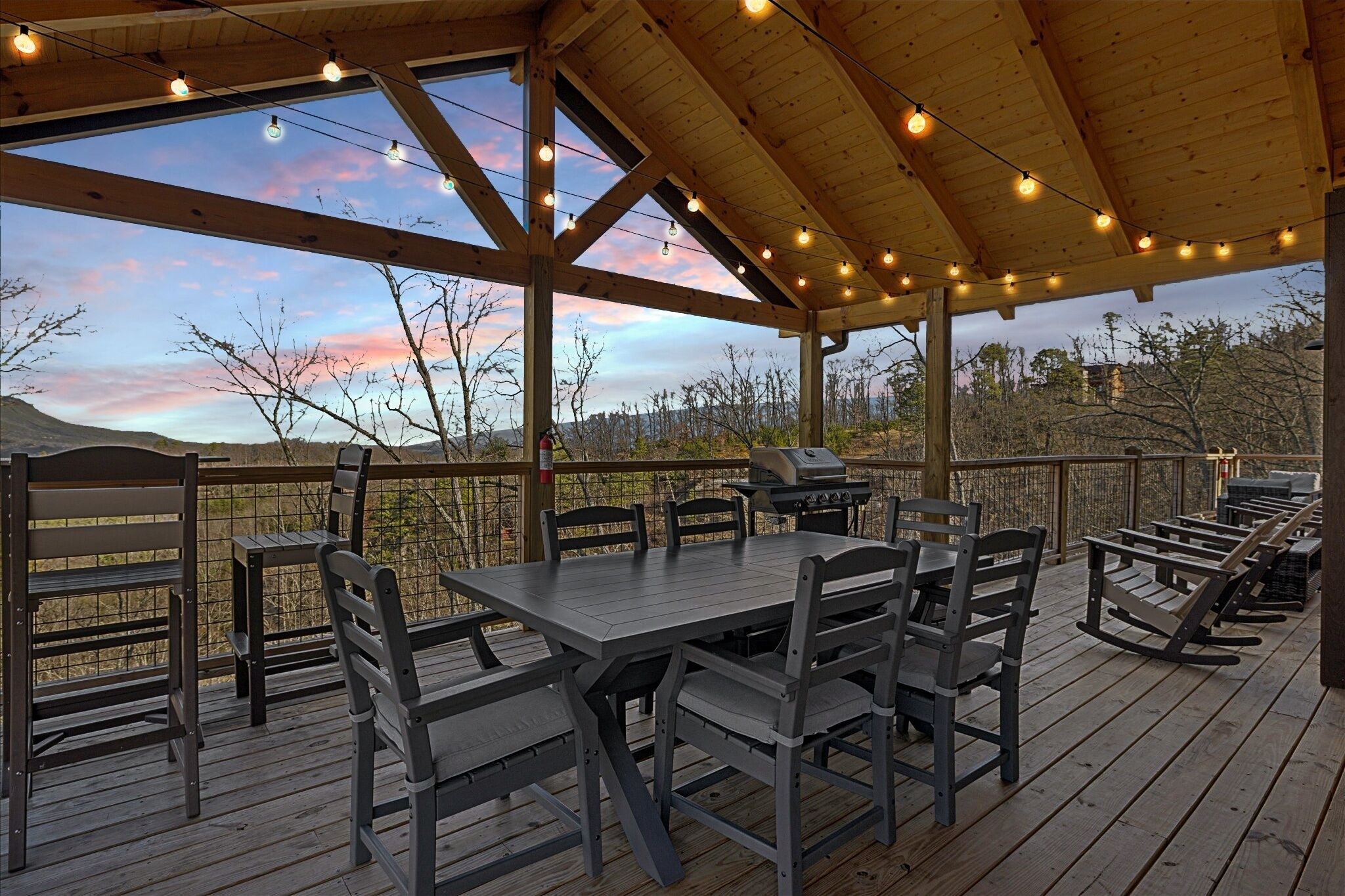 A covered outdoor patio with a table and chairs, a grill, and string lights.
