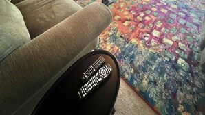 Una sala de estar con techo de madera, un ventanal grande, un tapete colorido, un sofá, una mesa de centro y un televisor montado en la pared.