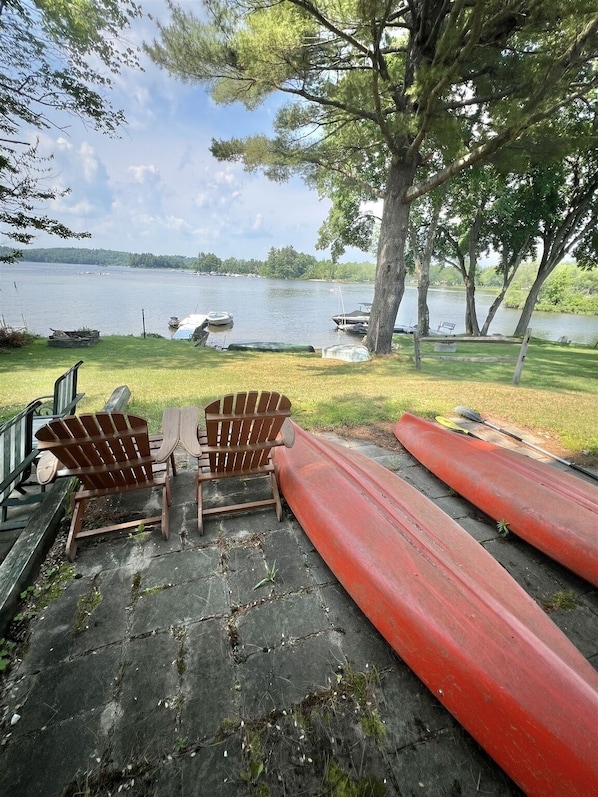A lakeside deck with Adirondack chairs, a canoe, and a kayak. - Sebago Escape Limit 12 5 Bedroom Home by RedAwning (Raymond)