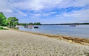 A sandy beach with boats on the water, trees, and a clear sky. - Sebago Escape Limit 12 5 Bedroom Home by RedAwning (Raymond)