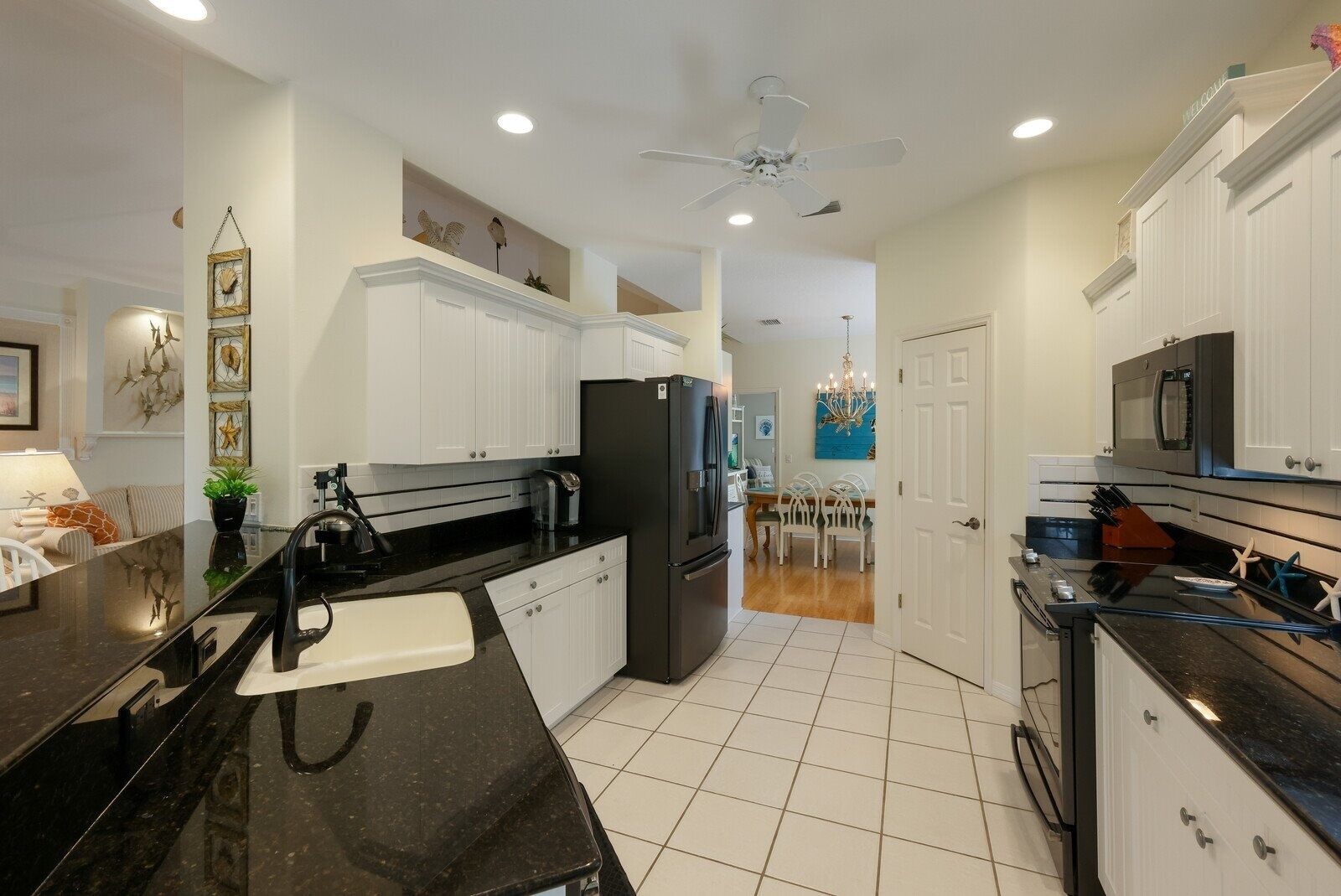 A modern kitchen with white cabinets, black countertops, a black refrigerator, and a dining area with a chandelier.