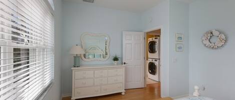 Un dormitorio con cama, cómoda y puerta que da a un cuarto de lavado.