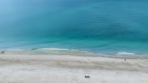 Een strand met helderblauw water en een zandkust.
