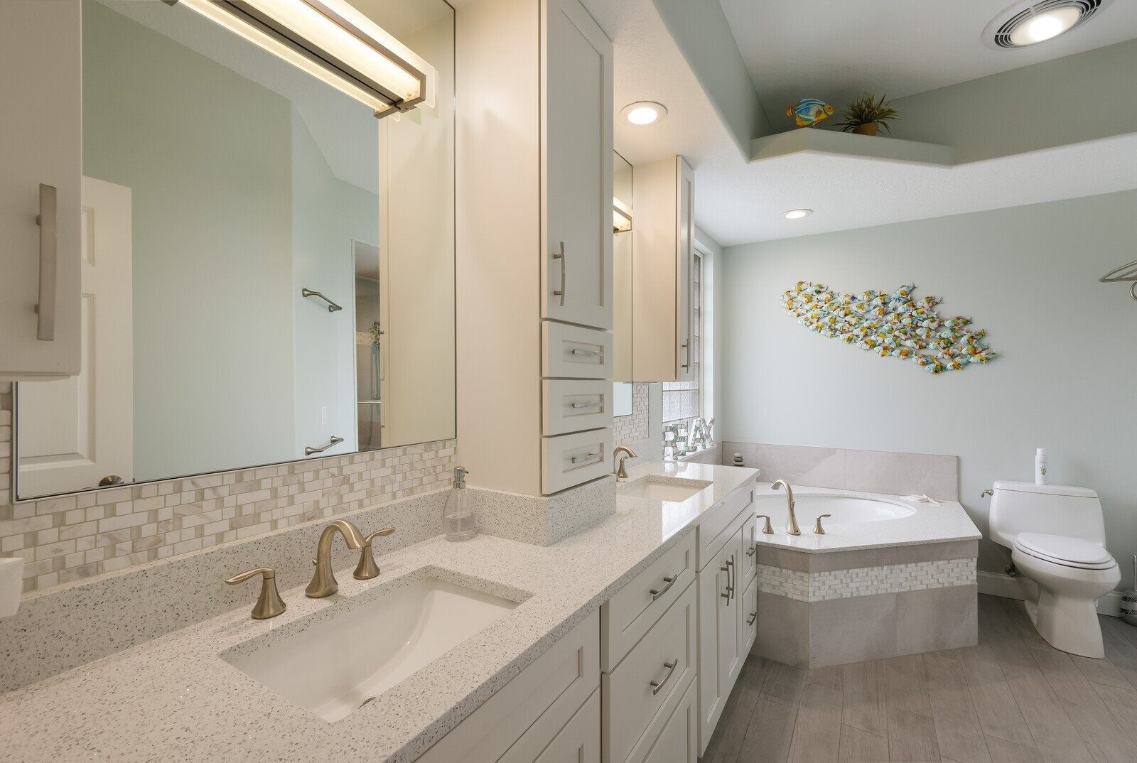 A modern bathroom with a large mirror, two sinks, a toilet, and a decorative wall piece.