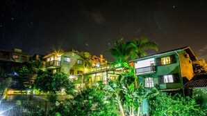 A multi-story residential building with balconies, surrounded by lush greenery and illuminated by artificial lighting. - Pousada Vale Verde Bungalows - Rosa (Imbituba)