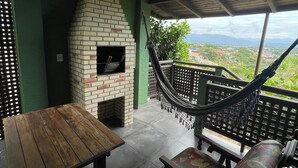 An outdoor patio with a brick fireplace, a hammock, and a view of the landscape. - Pousada Vale Verde Bungalows - Rosa (Imbituba)