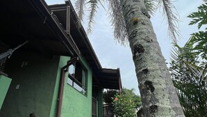 A house with a staircase leading to a porch, surrounded by greenery and a tall tree. - Pousada Vale Verde Bungalows - Rosa (Imbituba)