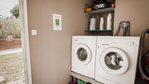 A laundry area with two front-loading washing machines, a shelf with bottles, and a sign on the wall. - La Cigalière Gite Rouge Cerise Avec Piscine et Salle de Sport Proche St Cyprien (ELNE)