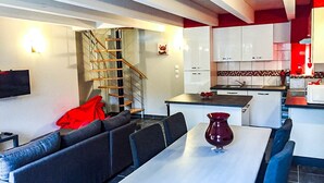 A modern kitchen with white cabinets, a red accent wall, and a dining area with a table and chairs. - La Cigalière Gite Rouge Cerise Avec Piscine et Salle de Sport Proche St Cyprien (ELNE)