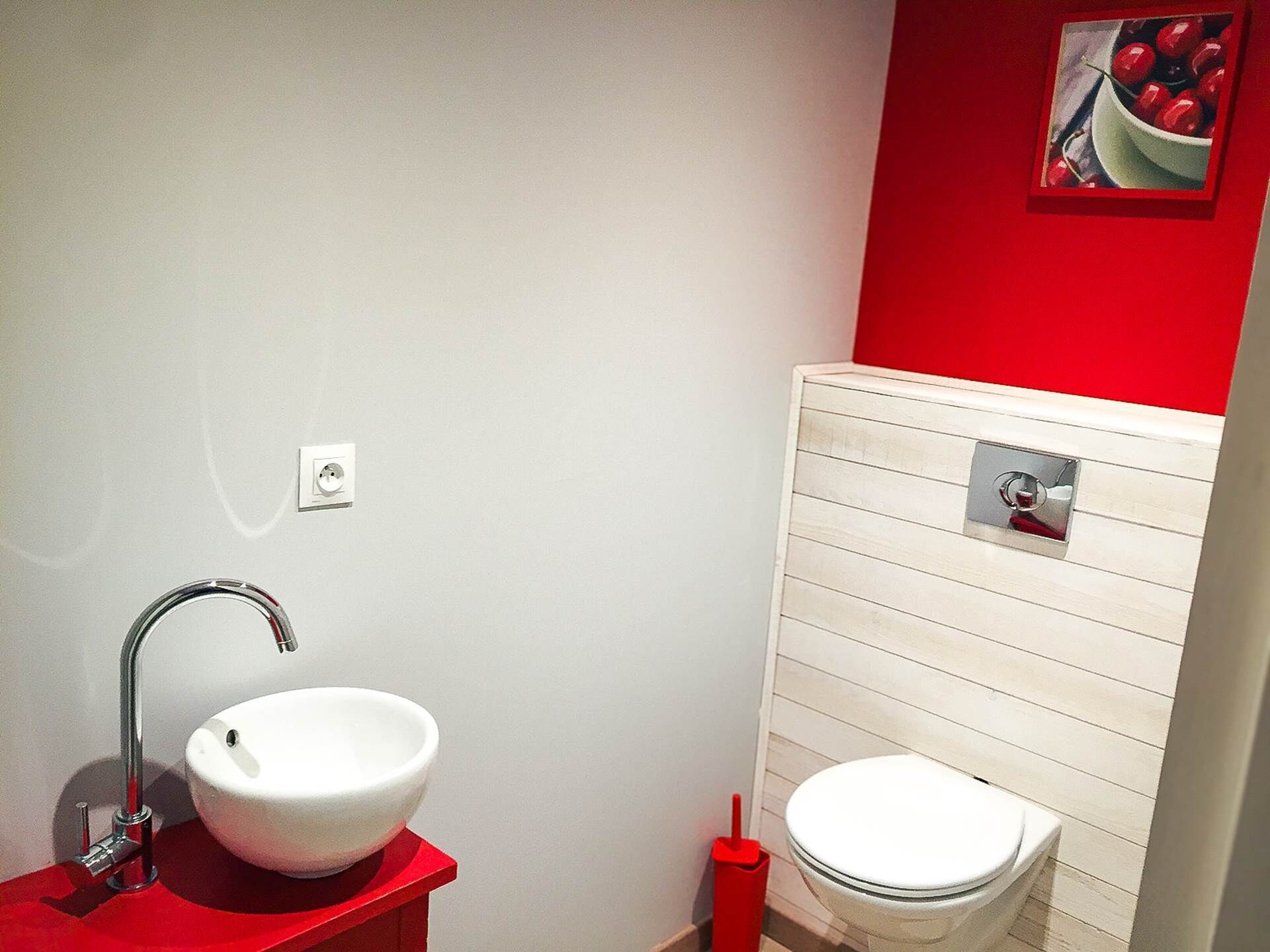 Une salle de bain avec un lavabo blanc, un plan de toilette rouge et des toilettes blanches.