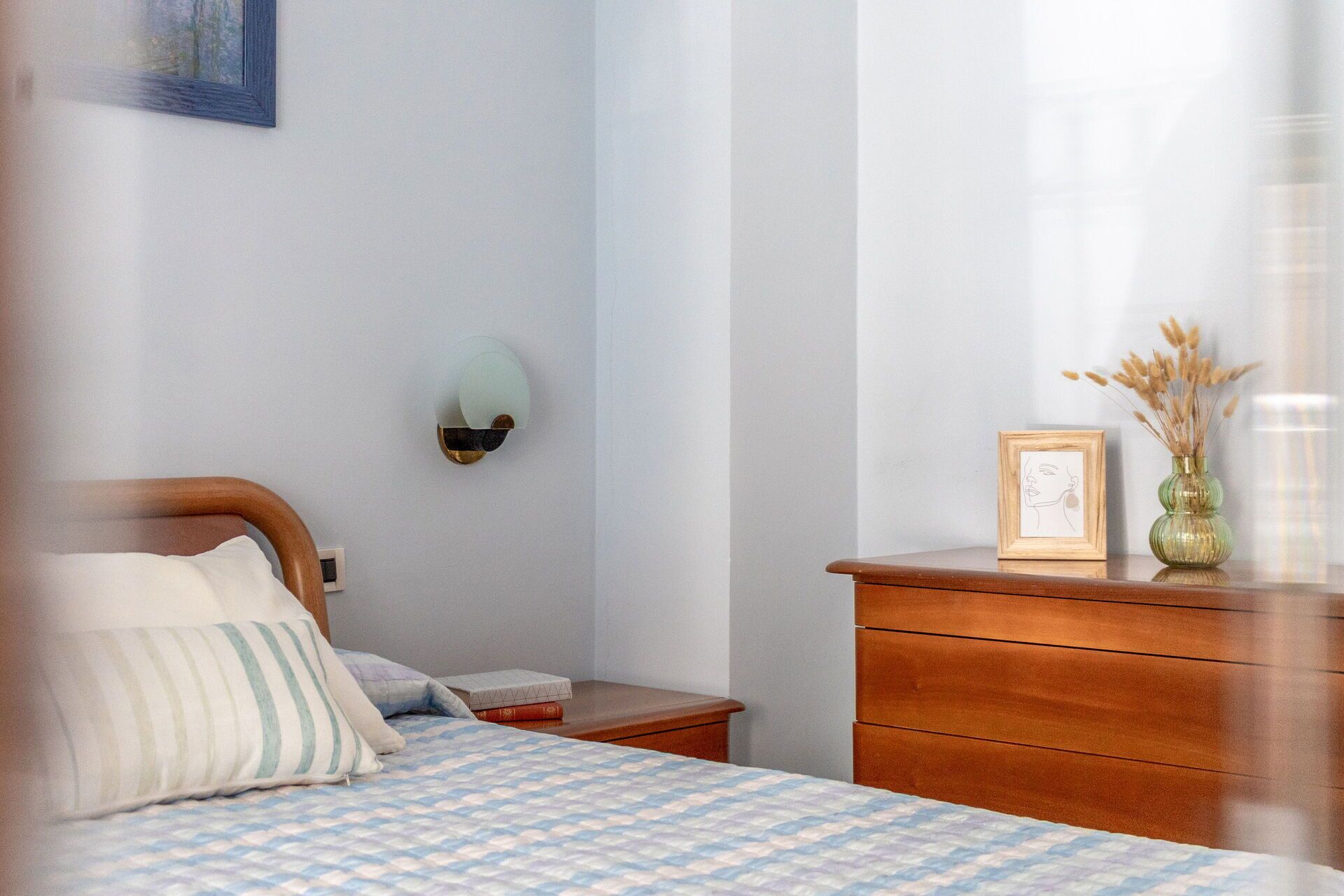 Een slaapkamer met een bed, nachtkastje, dressoir en een wandlamp.
