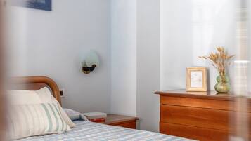 Een slaapkamer met een bed, nachtkastje, dressoir en een wandlamp.