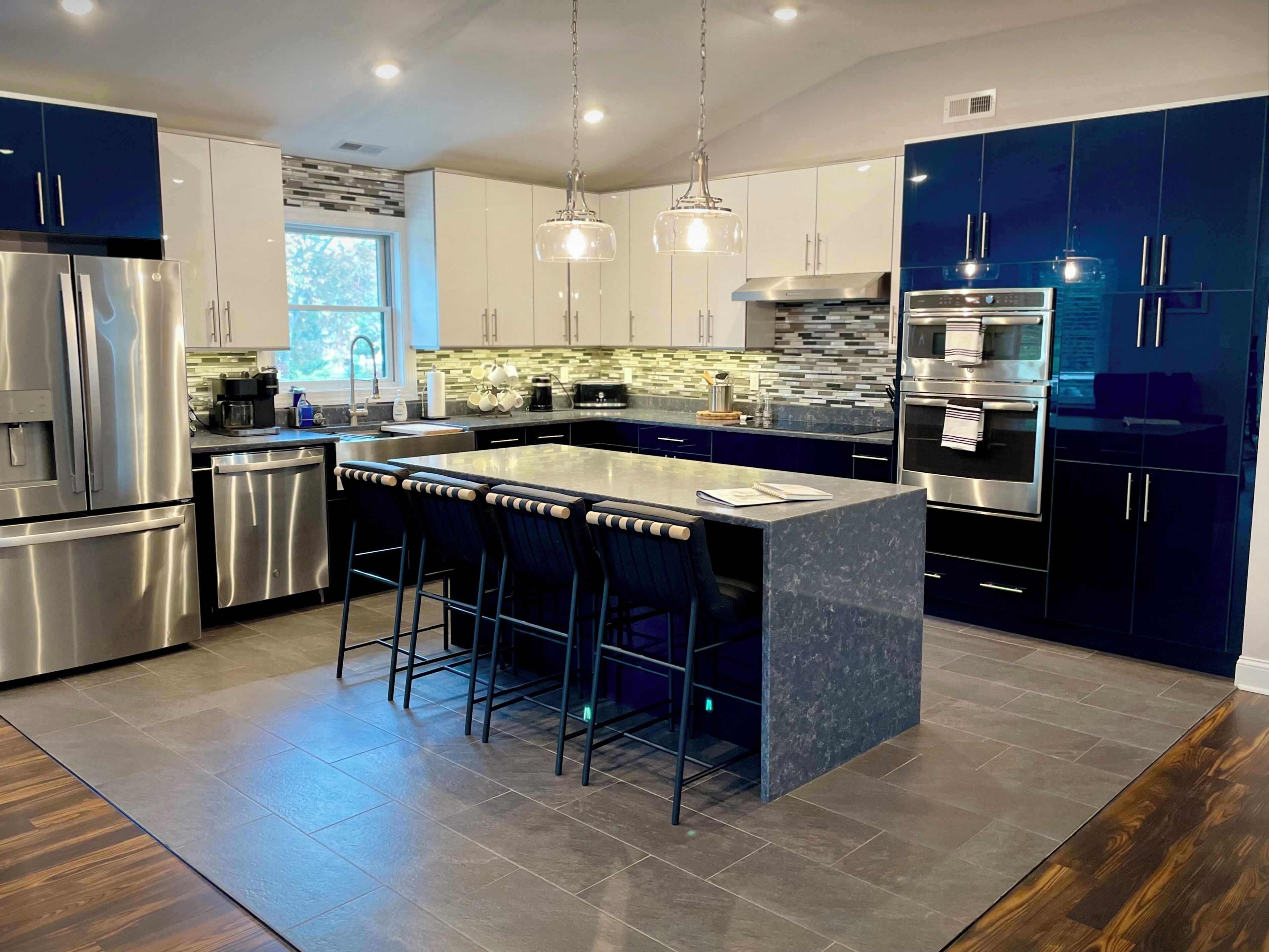 A modern kitchen with stainless steel appliances, a central island with bar stools, and dark blue cabinetry.