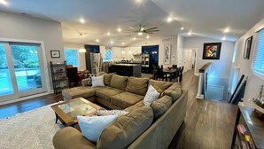 A modern living room with a sectional sofa, a glass coffee table, and a view of the backyard. - 6,000 Sq.ft. 18 Guests, 7-Bed, 6-Bath, Pool, Spa, Outdoor Kitchen, Garden, WIFI. (Middle Township)