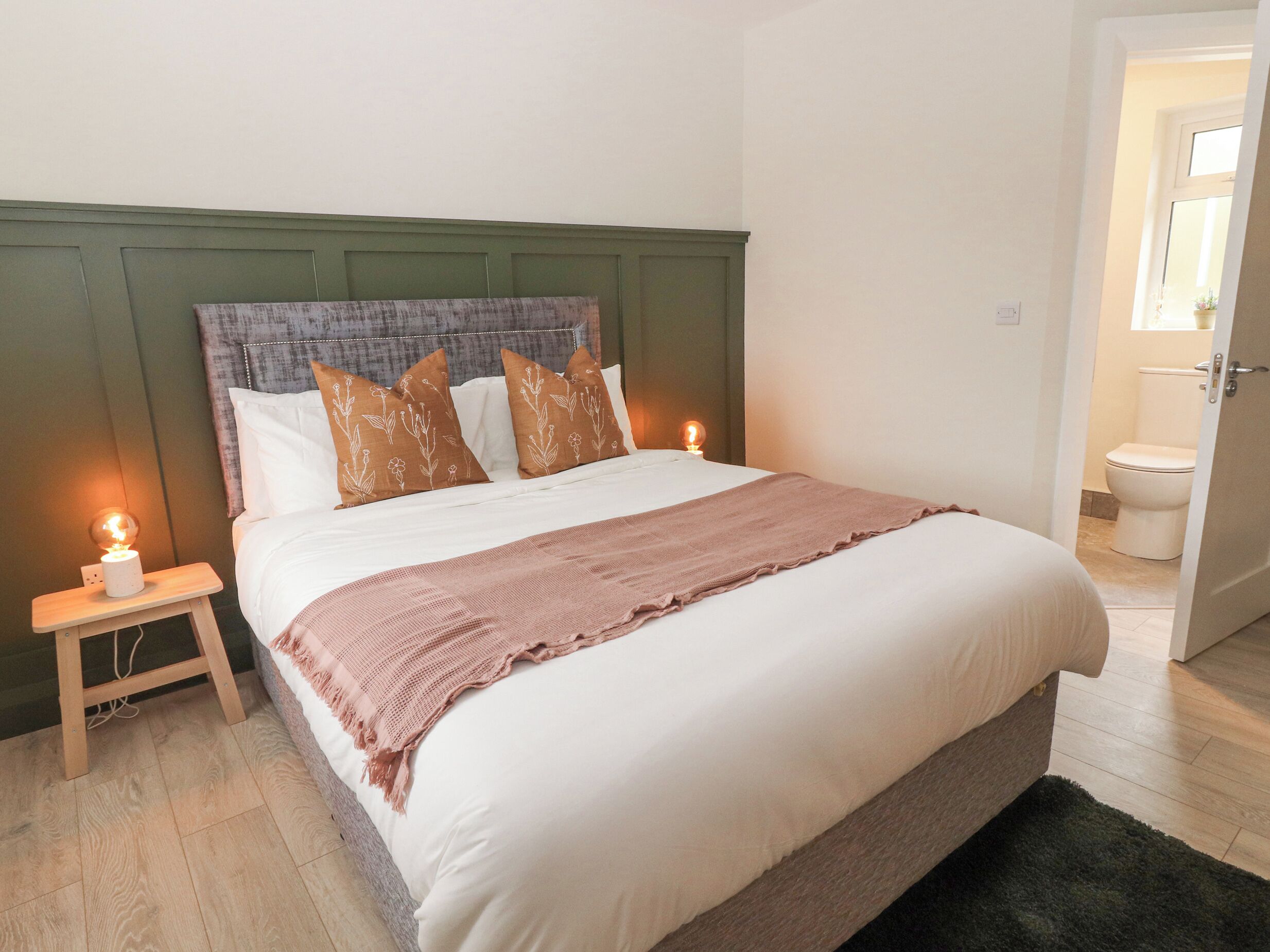 A neatly made bed with a white and pink blanket, a green headboard, and two bedside lamps.