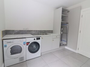 A compact laundry room with a washing machine, a dryer, a sink, and a shower enclosure.