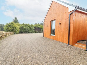 A modern wooden building with a gravel driveway and stone wall.