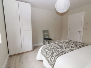 A bedroom with a bed, a wardrobe, a chair, and a hanging light fixture.