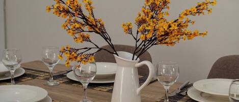 A dining table set with white plates, clear glasses, and a white pitcher with yellow flowers.