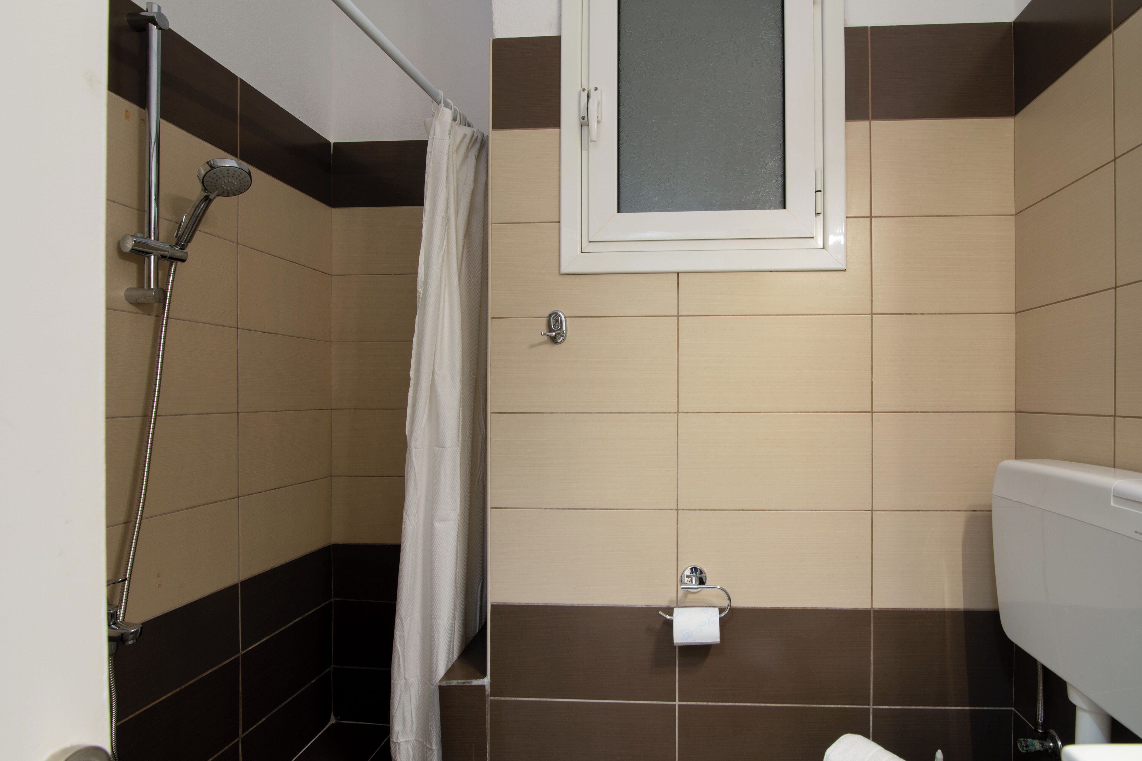 Un baño con ducha, inodoro y ventana.