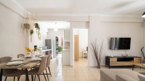 En moderne stue med sofa, fjernsyn og spiseområde med et bord dækket til fire personer.