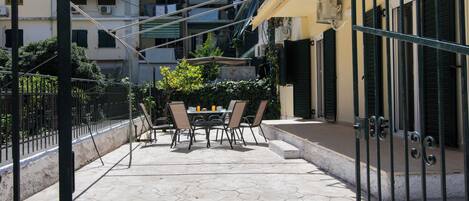 A courtyard with a table and chairs, surrounded by a metal fence and a building with shutters.